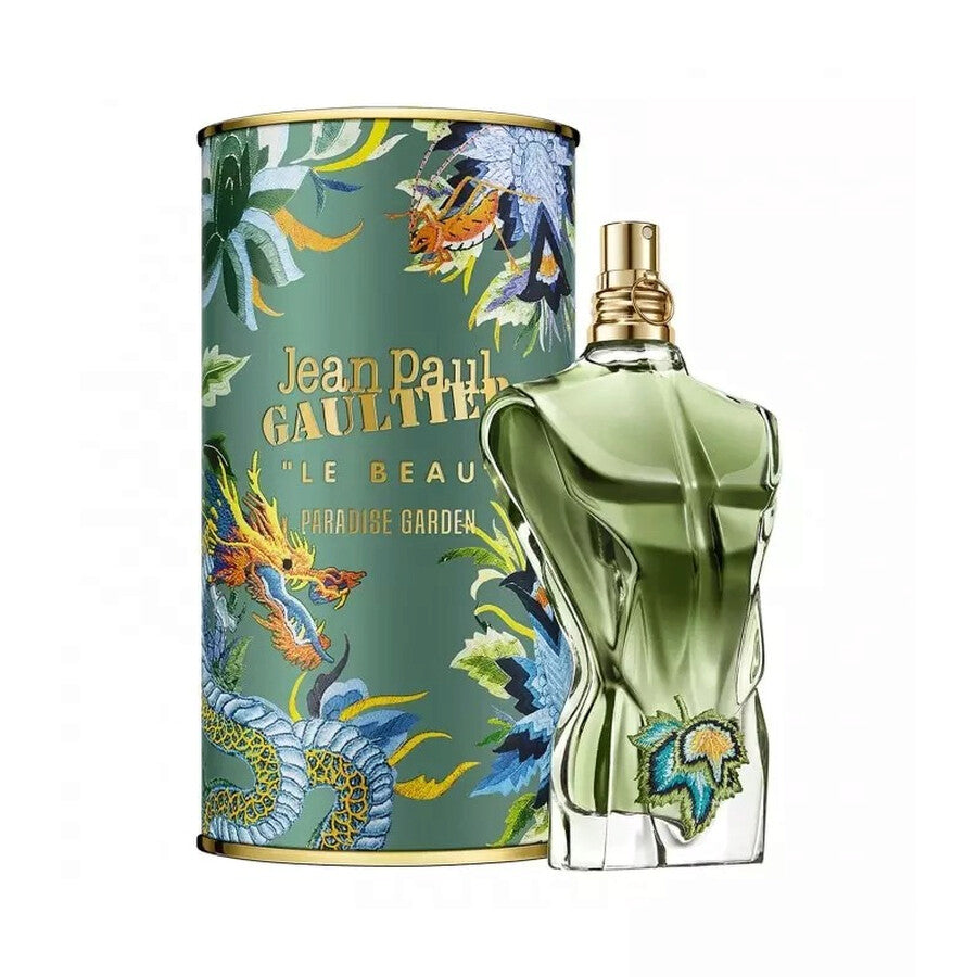 Un frasco verde con forma de torso masculino de JEAN PAUL GAULTIER LE BEAU PARADISE GARDEN 125 ML de DarlynS Perfumería y Accesorios se encuentra junto a una colorida caja cilíndrica decorada con un dragón y hojas tropicales.