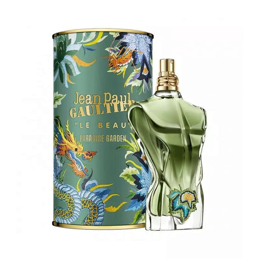 Un frasco verde con forma de torso masculino de JEAN PAUL GAULTIER LE BEAU PARADISE GARDEN 125 ML de DarlynS Perfumería y Accesorios se encuentra junto a una colorida caja cilíndrica decorada con un dragón y hojas tropicales.